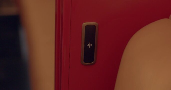 Tactile seat adjustment button on red jet panel next to leather seating. Detailed view of tactile control button situated on red panel near leather seat in cabin