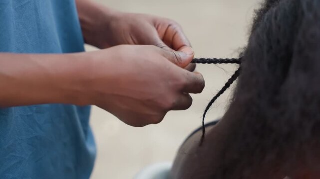 Street scene with hairstyling activity. Individual securing braid tips during lively city street moment. Person carefully fixing hair in bustling city street setting as others observe