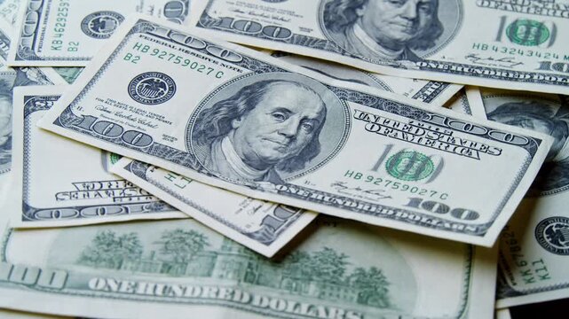 Colorful stacks of hundred dollar bills gracefully spread across a soft surface. The crisp notes showcase intricate designs, creating a visual feast under warm light