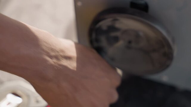 Black carpenter adjusting router knob for depth setting turning dial on metal base closeup of veined hands and grip tape measure at edge workshop sunlight machine maintenance practical focus