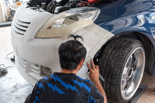 Mechanic sanding and repairing car front bumper in auto garage open hood visible automotive bodywork maintenance and restoration process close up detail