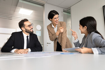 Multiethnic team members gather at table with charts, engaging in positive business collaboration during informal meeting, smiling, finding solution, making decision, enjoy friendly office teamwork