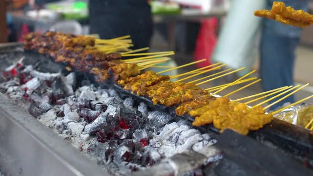 Satay meat skewers grilling over hot charcoal embers at street food stall.