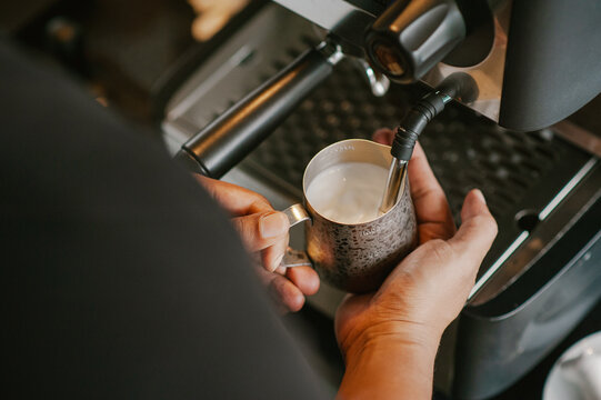 Barista steaming milk in stainless steel pitcher for coffee latte