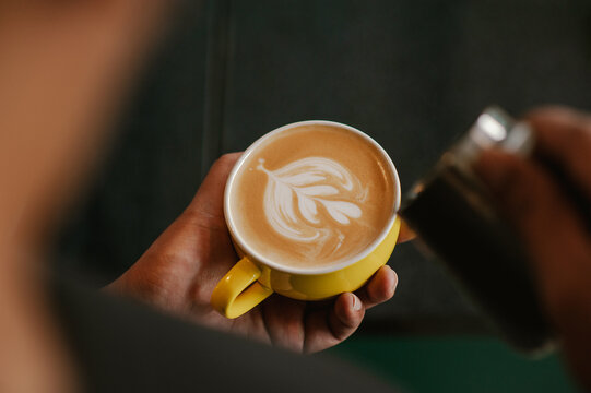 Barista holding a yellow cup of coffee latte with heart latte art