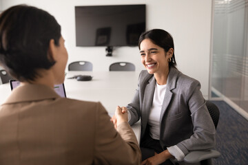 Smiling adult 30s businesswoman shaking hands with female business partner after successful teamwork, office meeting or negotiations in conference room. Partnership, closing deal, gesture of agreement