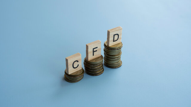 CFD letters on wooden tiles placed on stacks of gold coins for contract for difference trading and financial investment concept.
