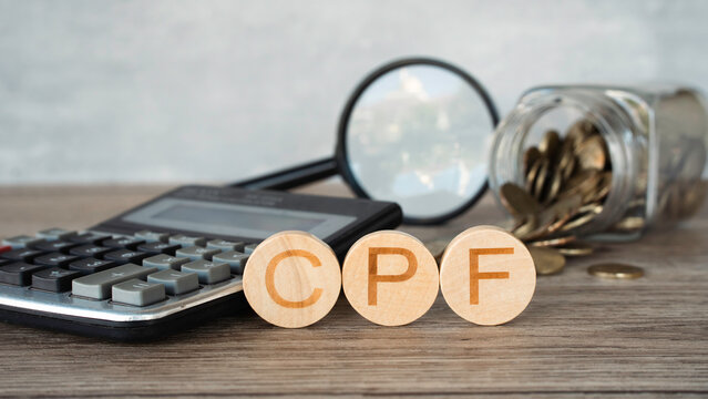 Central Provident Fund CPF word on wooden blocks with calculator and coins jar background.
