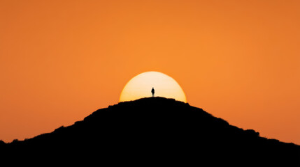 Obraz premium person stands alone on a hilltop silhouetted against a large orange sunset, evoking solitude and nature