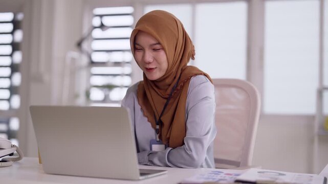 Asian adult professional woman engaging in virtual video conference on laptop at modern office workplace communication technology