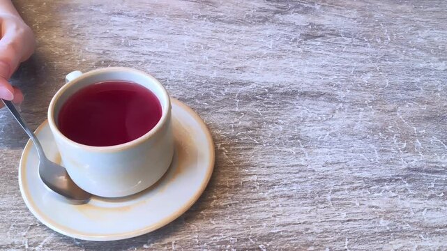 cup of red tea with spoon on rustic wooden table hand touching cup cozy cafe drink closeup simple composition warm light concept of cafe business restaurant hospitality