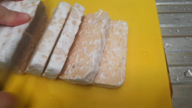 Cutting Tempeh for Cooking Preparation&ndash;Indonesian Fermented Soybean Food. Close-up video of cutting fresh tempeh into slices for cooking preparation.The video highlights food preparation