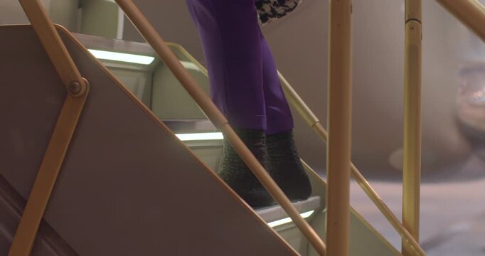 Passenger ascending jet stairs in purple uniform, black boots on illuminated steps, brass railing and cabin interior visible, closeup detail of climb and motion capturing boarding