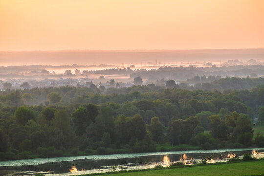 Green fields and meadows with trees and river at pink foggy sunrise. Beautiful summer landscape.