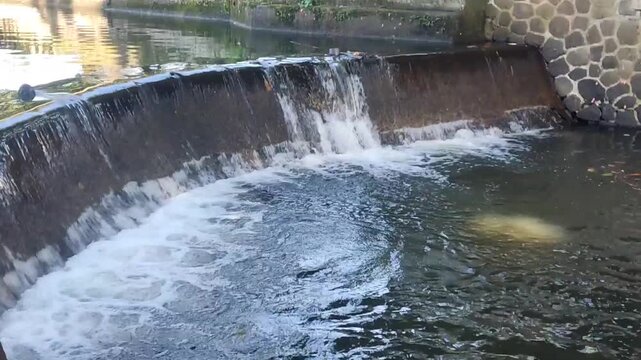 A small river dam with fast-flowing water below is used for irrigation in a rural area