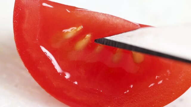 Close up motion of a knife slicing through juicy red tomato segment revealing seeds and pulp.