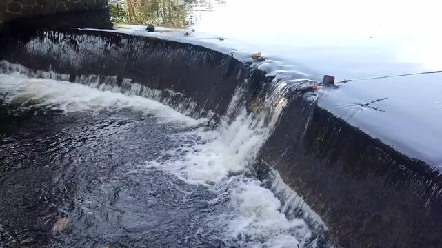 A small river dam with fast-flowing water below is used for irrigation in a rural area