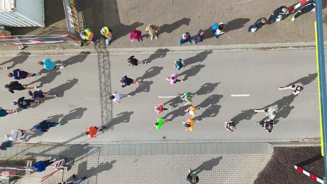 Aerial drone view of people running half marathon race in city, shadows of runners on road racing sport competition, top-down view of athletes and spectators