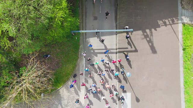 Aerial drone view of people running half marathon race in city, shadows of runners on road racing sport competition, top-down view of athletes and spectators