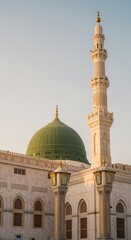 Obraz premium Islamic Architecture Details Featuring a Large Green Dome and Tall Minaret Against a Clear Sky for Religious Pilgrimage Guide and Historical Archive Content