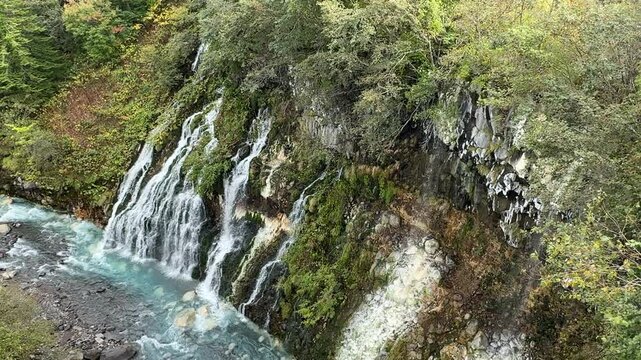 Shirahige Waterfall with deep cobalt blue hue, Waterfall of Shirahige and Tokachidake Mountain Range in Biei-cho, Hokkaido Japan in early fall or autumn season. famous tourist destination in Biei