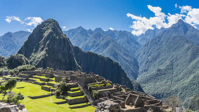 The famous Lost City of the Incas Machu Picchu. Dilapidated stone buildings, stairs, green terraces. Silhouettes of people walking. The Andes mountain range, Huayna Picchu, blue sky, clouds. Peru.