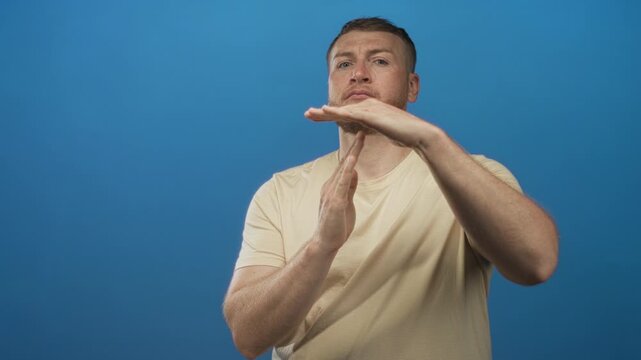 Young heavyset man with hands forming timeout gesture in bright blue studio setting, visible forearms and neutral expression; seriousness.