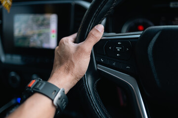 Close-up of Man’s Hand on Steering Wheel Driving a Modern Car with Navigation Map,A detailed close-up shot of a person's hand holding a leather steering wheel while driving. The background shows. © banjongseal324