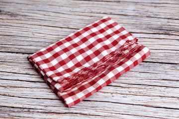 Obraz premium Red and white checkered cloth napkin rests on wood. Folds show soft texture and gentle creases. Rustic background adds charm and nostalgia. Ideal for kitchens, cafes, or picnic scenes