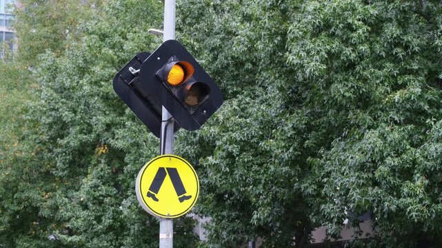 an amber orange traffic light signal and distinctive yellow circular pedestrian crossing warning sign mounted on a pole in Melbourne Australia.&nbsp;Pedestrian sign features walking legs symbol