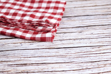 Obraz premium Red and white checkered cloth napkin rests on wood. Folds show soft texture and gentle creases. Rustic background adds charm and nostalgia. Ideal for kitchens, cafes, or picnic scenes