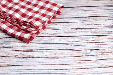 Obraz premium Red and white checkered cloth napkin rests on wood. Folds show soft texture and gentle creases. Rustic background adds charm and nostalgia. Ideal for kitchens, cafes, or picnic scenes