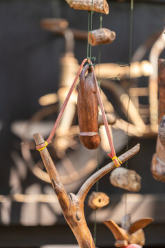 Intricate wooden phallic carving displayed on strings, featuring traditional craftsmanship. The warm tones of the wood and natural textures evoke cultural artistry. Blurred background.