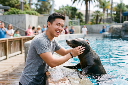 Happy young asian man smiling while petting sea lion in outdoor marine park pool