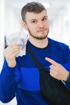 A young man in a blue sweater displays cash while pointing, conveying a sense of confidence and financial success in a contemporary environment.