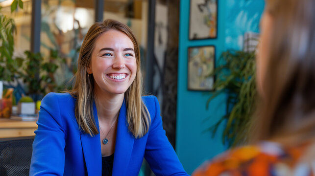 A candid shot of a smiling professional woman in a blue jacket having a discussion in a creative workspace,