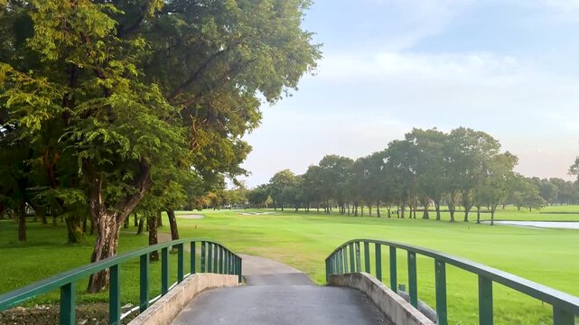 Smooth gliding shot over bridge into lush green golf course, bright sunny day, perfect for cinematic golf or nature footage.