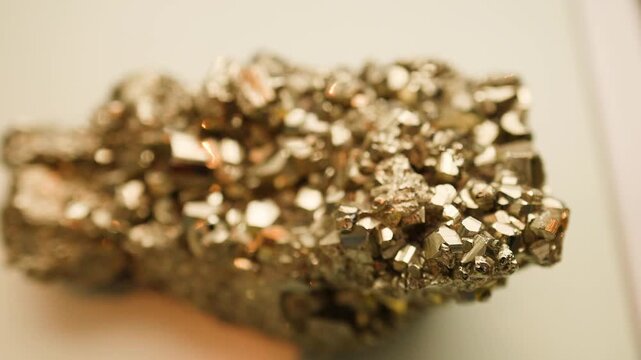 Cinematic close up of golden pyrite mineral cluster with metallic crystal structure shimmering under soft light.