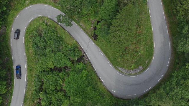 Aerial view of winding forest road with multiple vehicles navigating sharp curves in nature