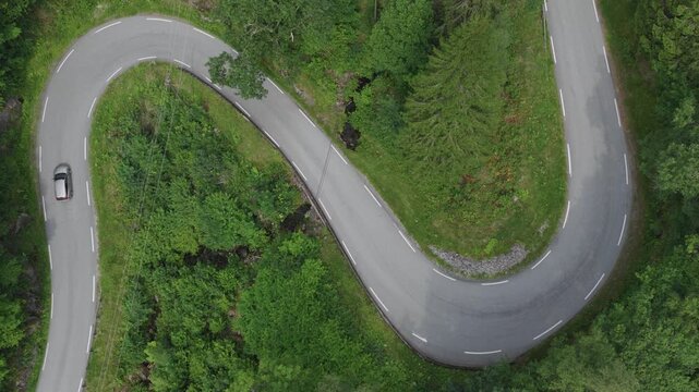 Top down aerial of sharp forest road curve with vehicle navigating narrow asphalt path