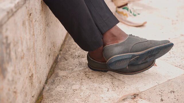 Father shoes resting on stone steps, adult loafer crossed over step, sons sneaker peeking blurred in background, formal trousers and textured concrete, gentle midday light, quiet paternal moment