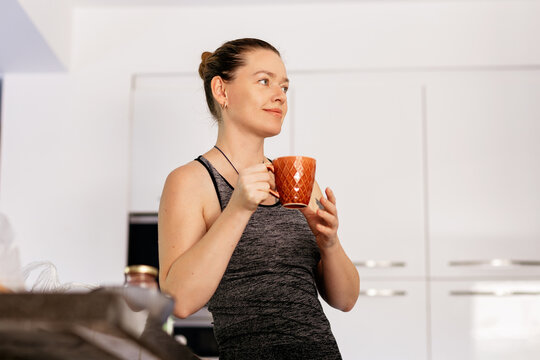 Young woman in grey sportswear drinking coffee in the kitchen