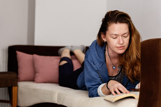 Young woman in sportswear lying on a sofa and reading a book