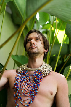Man with beaded necklace looking up among tropical plants, Bali