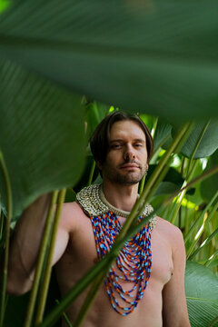 Man with multicolored beaded necklace among tropical leaves