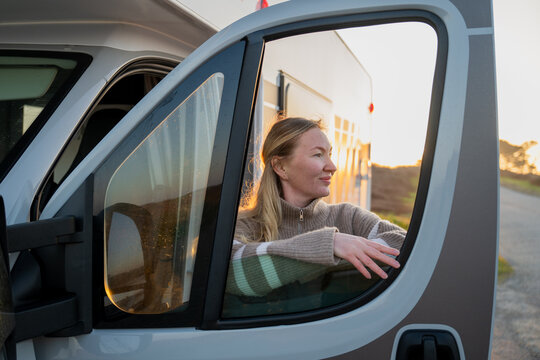Woman inside campervan watching sunset by ocean during travel journey