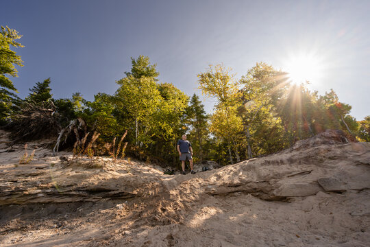 Man hiking up sandy beach hill in Pictured Rocks with sunburst