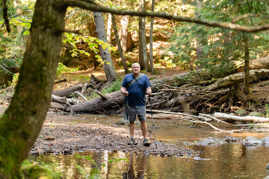 Middle-aged man hiking with trekking poles crossing a Michigan creek