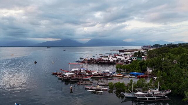 Static aerial view of a traditional fisherman village with stilt houses docked bangka boats mangroves and distant mountain range along calm bay in Puerto Princesa Palawan Philippines
