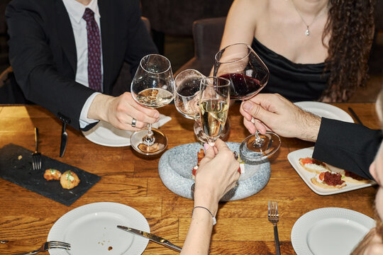 Young adult friends clinking wine glasses over restaurant table during group dinner, celebrating social connection and nightlife spending. Ideal for hospitality marketing and event promotion